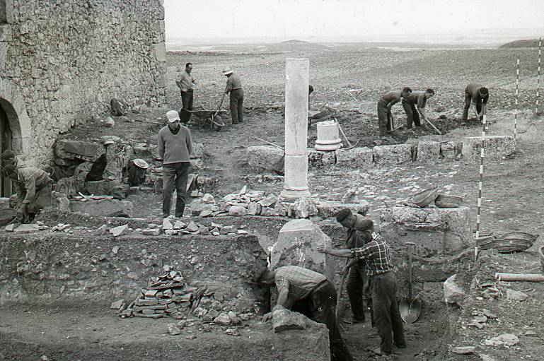 [Vista general de la zona d'excavació prop d'una construcció moderna, amb dos columnes i els treballadors a Clunia]