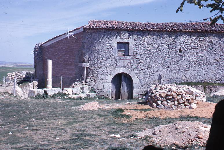 [Vista general de l'edifici conservat en elevació entre les runes de Clunia]